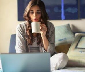 A woman drinking from a mug while using her laptop